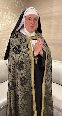 a nun in a black robe standing in front of a couch