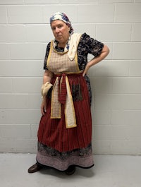 a woman in an old apron posing in front of a wall