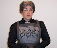 a woman in an apron standing in front of a white wall
